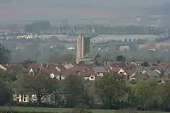 Multiple houses with prominent square tower. Hills in the background.