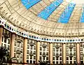 Interior of a domed atrium surrounded by hotel rooms and tall columns with light coming in through blue windows