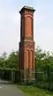 A chimney-like brick structure in two stages with some brick decoration and a corbelled top