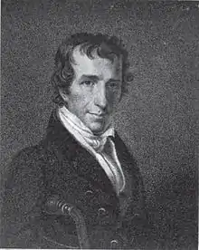 A man with dark, curly hair wearing a white shirt and black jacket