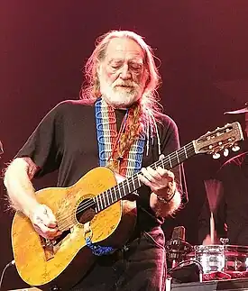 A man with long white hair and a beard playing a guitar