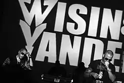 Two young men performing in front of large "Wisin & Yandel" background