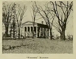 Historical photograph of Woodside Mansion with trees surrounding it.  The front of the house has six columns in the Doric style, two stories tall.  The ground slopes up gently from the photographer's location to the building.