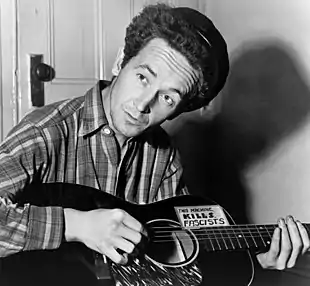 Guthrie playing guitar and looking up at an angle away from the camera in a black-and-white photo