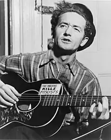 Woody Guthrie, half-length portrait, facing slightly left, holding guitar