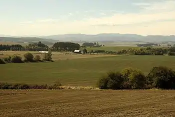 Farm fields spread into the distance, where a barn and far-off mountains can be seen