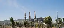 white smoke rises into a blue sky from 3 large chimneys