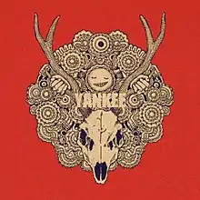 A black and white drawing of a deer's skull with large antlers on a red background, in the middle of a round pattern with many patterned circles. Above the skull is a smiling face, with two hands holding onto its antlers. In the middle of the pattern are the letters "YANKEE" written in white.