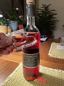 A hiking boot shot glass filled with red-ish pine liqueur in front of a whole bottle of pine liqueur on a table