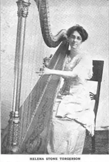 A white woman wearing glasses, her hair in an updo, seated at a harp.