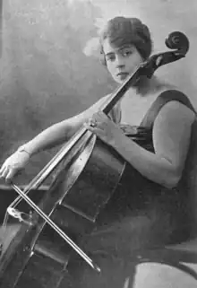 A woman wearing a dark gown, seated, holding a cello and bow.