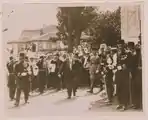 The Caliph walking with entourage of soldiers, officials and a brass band as women watch