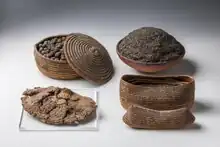 Seeds and fruit in coiled baskets and a bowl, and a large loaf of bread