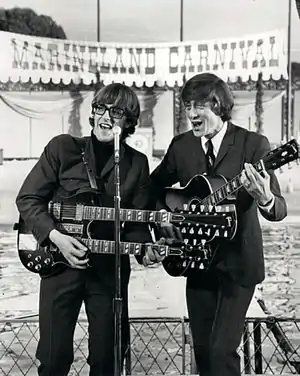 Chad and Jeremy standing at a microphone, singing and playing guitars