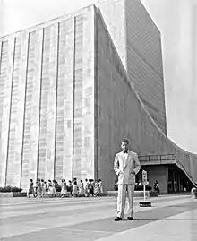 A man stands infont of a modern curved roof building.