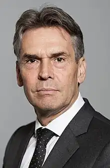 A Caucasian man in suit looking at the camera in front of a grey background