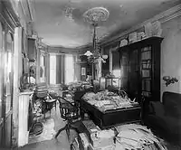 This picture is of a room with bookcases against the walls and two Louis-the-16th style desks in the middle of the room. Old mail is piled on the desks and on the floor by the desks.