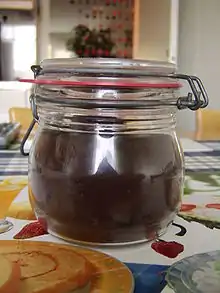 small squashed looking Jar filled with dark purplish-red jam with a metal lock on the lid