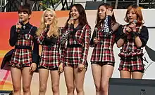 Image of Ladies' Code members holding microphones and wearing matching black, red and white plaid outfits