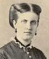 Photographic portrait of a young lady with dark-colored hair swept back and wearing a high-necked, Victorian era striped dress, dark earrings and a dark locket suspended around her neck on a ribbon