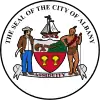 Circular seal with central images of a shield at center and sailing ship above it, with a European man to the left and a Native American to the right. The seal's edge reads "THE SEAL OF THE CITY OF ALBANY" with "ASSIDUITY" in a banner above the bottom.