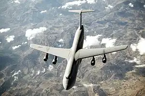 Top view of four-engine jet transport in-flight above mountain range.