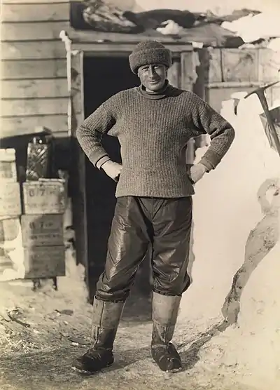 Photo of a man in a jaunty pose outside a hut