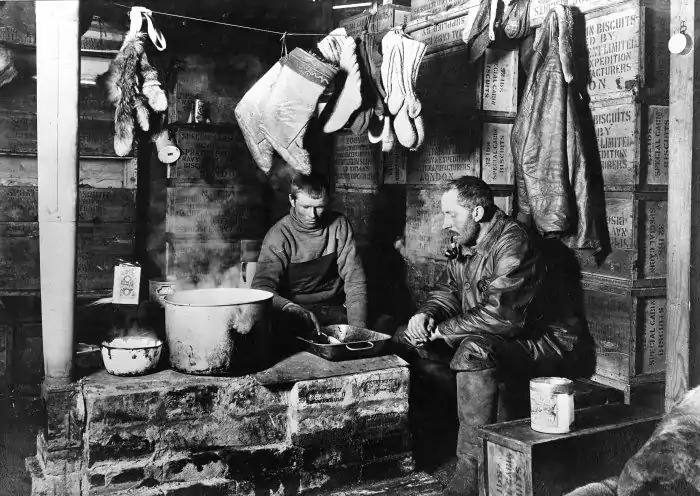 Photograph of two men sitting around a steaming basin inside a hut