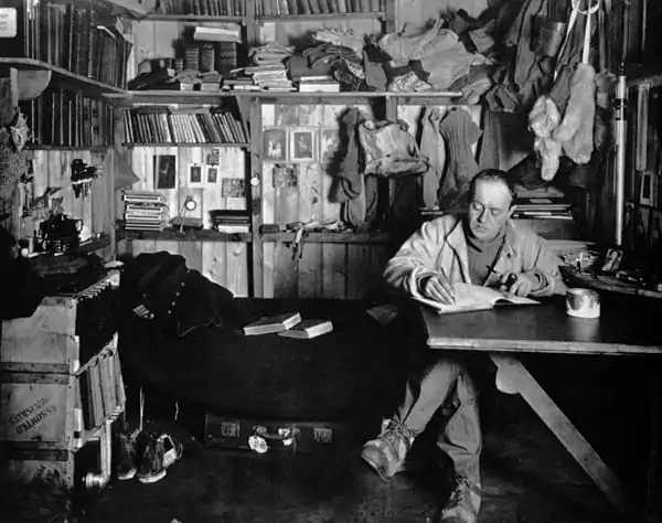 Photo of Scott seated at a table in a wooden room with crowded but tidy shelves of books and cold weather gear