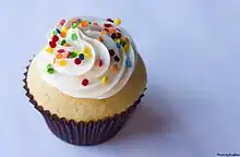 A photograph of a cupcake with white frosting and multicoloured sprinkles.