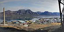 Longyearbyen with coal power plant and industrial buildings in the foreground with the fjord and bare mountains behind.