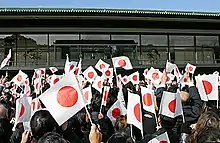 A group of people wave Japanese flags at a palace.